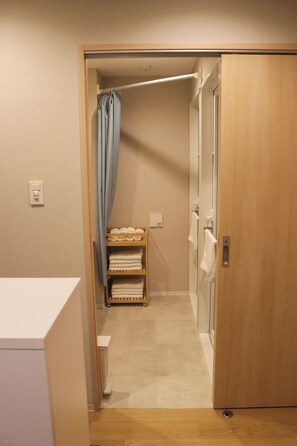 Corredor estreito que dá para um quarto com porta de madeira, porta-toalhas com toalhas dobradas e um interruptor de luz na parede.