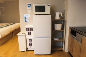 Uma kitchenette compacta com micro-ondas, frigorífico e uma pia pequena.