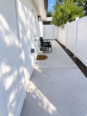 A concrete patio with a white fence, two chairs, and a door with a doormat. - Ensueño Luxery Pet-Friendly/Near Busch Gardens & USF /Your PerfectTampaGetaway (Tampa)