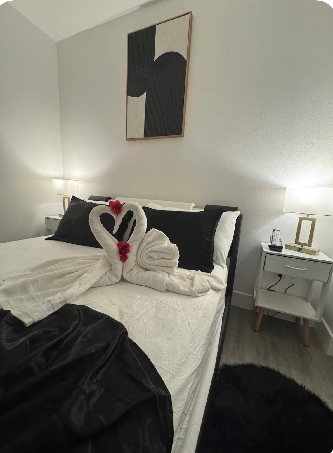 A hotel room with a bed, a bedside table with a lamp, and a wall-mounted artwork.