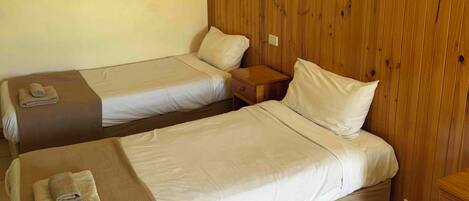 A room with two single beds, wooden paneling on the wall, a small wooden nightstand, and a tiled floor.