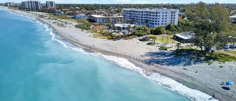 A coastal hotel with a beach view, multiple floors, and a mix of residential and commercial buildings in the background.