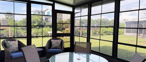 A sunroom with a glass ceiling, large windows, a round table, and wicker chairs.