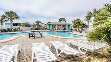 Piscina com espreguiçadeiras e mesa de piquenique, cercada por palmeiras e edifícios.