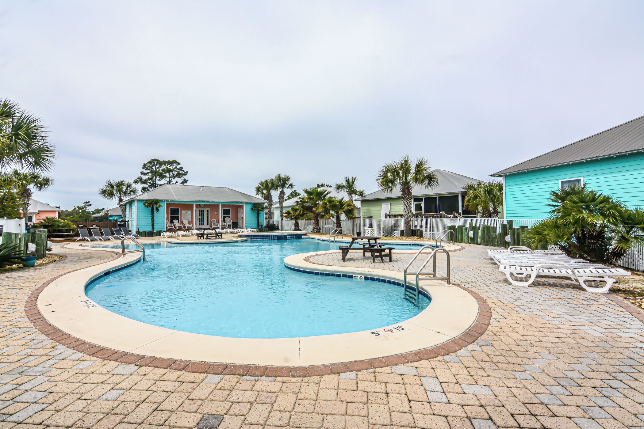 A swimming pool with a tiled deck, lounge chairs, and a small building with a porch.