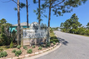 A sign for The Rookery III with a bird logo, surrounded by trees and a clear sky. - 5003 Rookery 3 The Sea Pearl (Gulf Shores)
