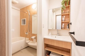 A modern bathroom with a bathtub, shower, and a vanity with a mirror and shelves. - NIKYO Taisho No1 Private Villa OSAKA (Osaka)