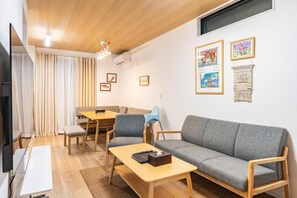 A modern living room with a sofa, a coffee table, a dining table, and chairs. There are framed pictures on the wall. - NIKYO Taisho No1 Private Villa OSAKA (Osaka)