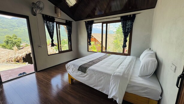 Un dormitorio con cama, piso de madera y ventanas grandes con cortinas.