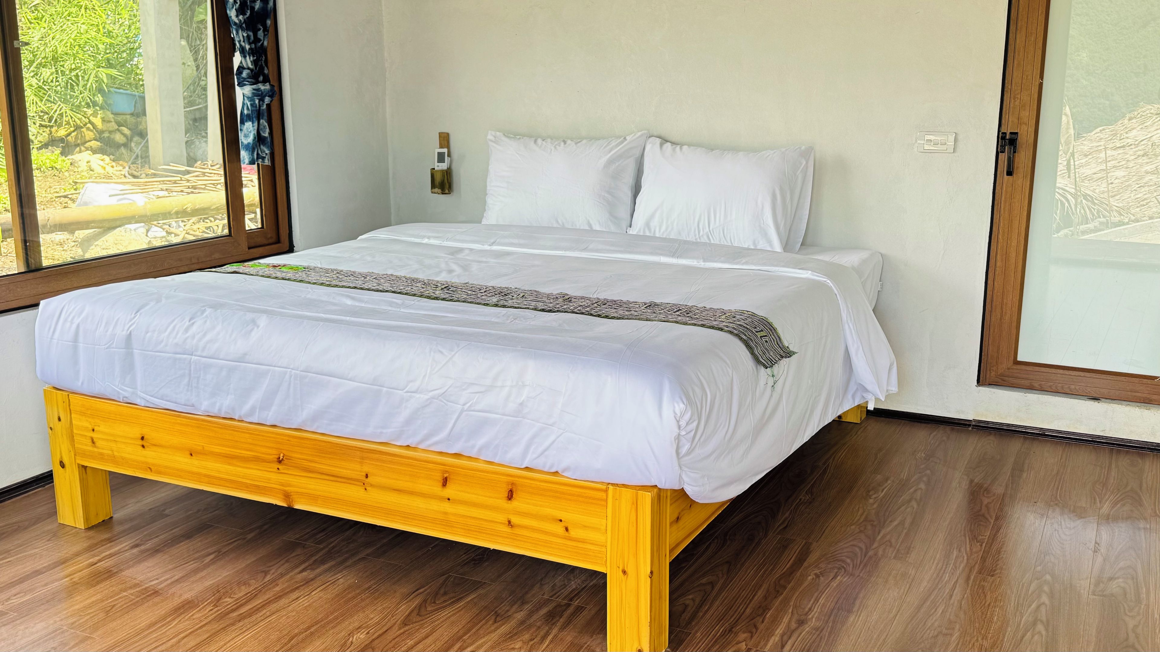Una cama con ropa de cama blanca, cabecera de madera y un plaid estampado.