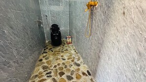 Un área de ducha pequeña con azulejos, un cabezal de ducha manual y un objeto negro en el suelo.