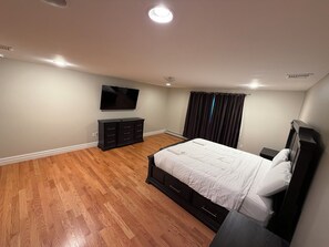 A bedroom with a bed, a dresser, a television, and a window with curtains.