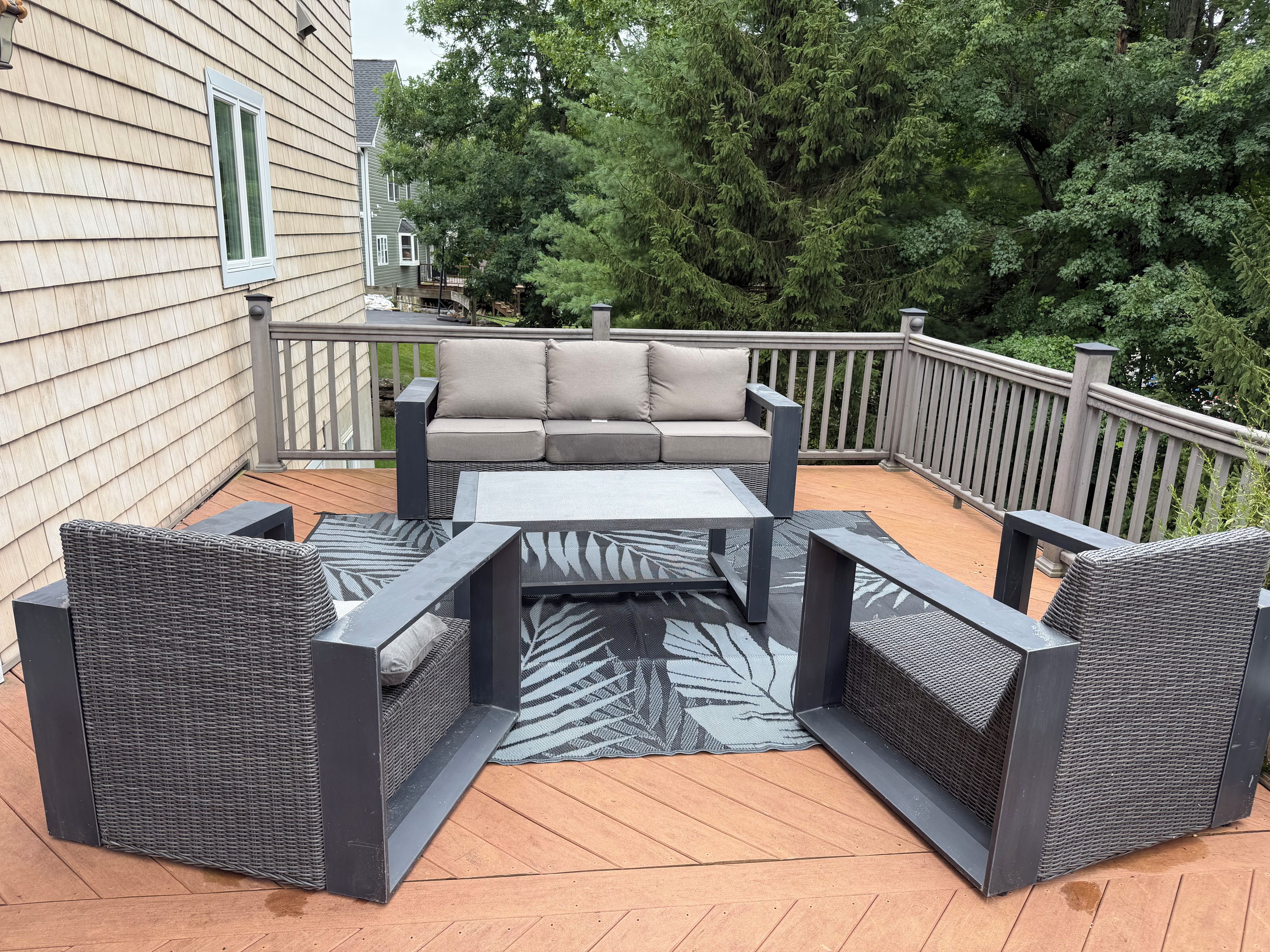 An outdoor patio with a sofa and chairs, a small table, and a patterned rug.