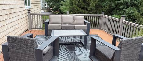 An outdoor patio with a sofa and chairs, a small table, and a patterned rug.