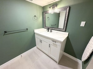 Un baño con tocador blanco, un espejo grande con marco decorativo y un perchero en la pared.