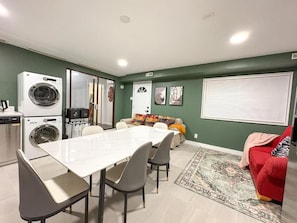 Un espacio habitable compacto con comedor, un sofá, un sillón rojo, lavadora y ventana con persianas.