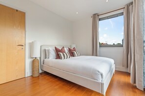 A bedroom with a bed, a bedside lamp, a window with curtains, and a wooden floor. - City View Duplex with Jacuzzi & Snooker Sleeps 10 (London)