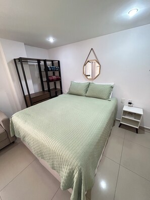 Een slaapkamer met een bed, nachtkastje, kledingkast en een spiegel aan de muur.