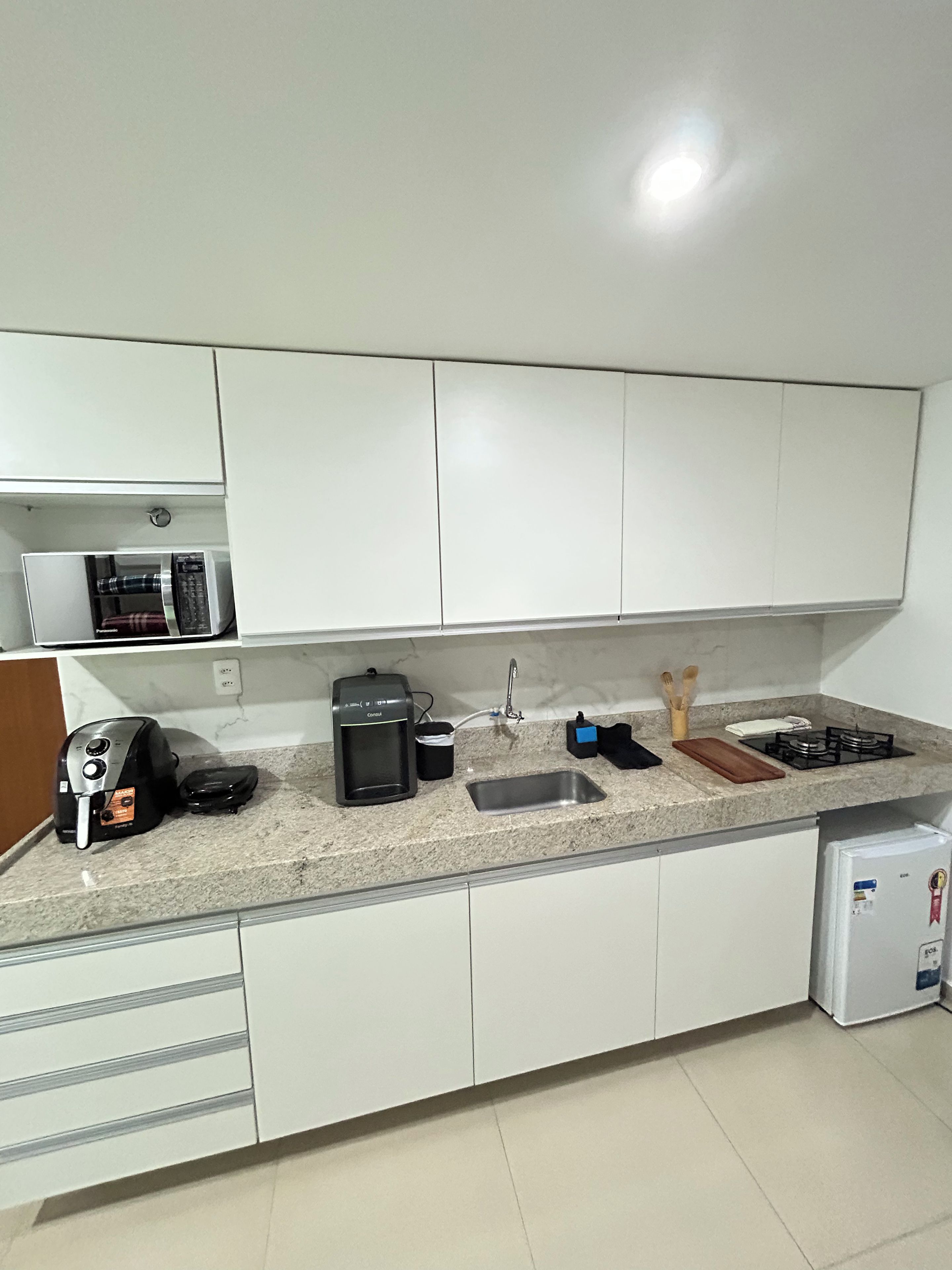 A kitchen with white cabinets, a countertop, a coffee maker, a kettle, a toaster, a sink, and a small refrigerator.