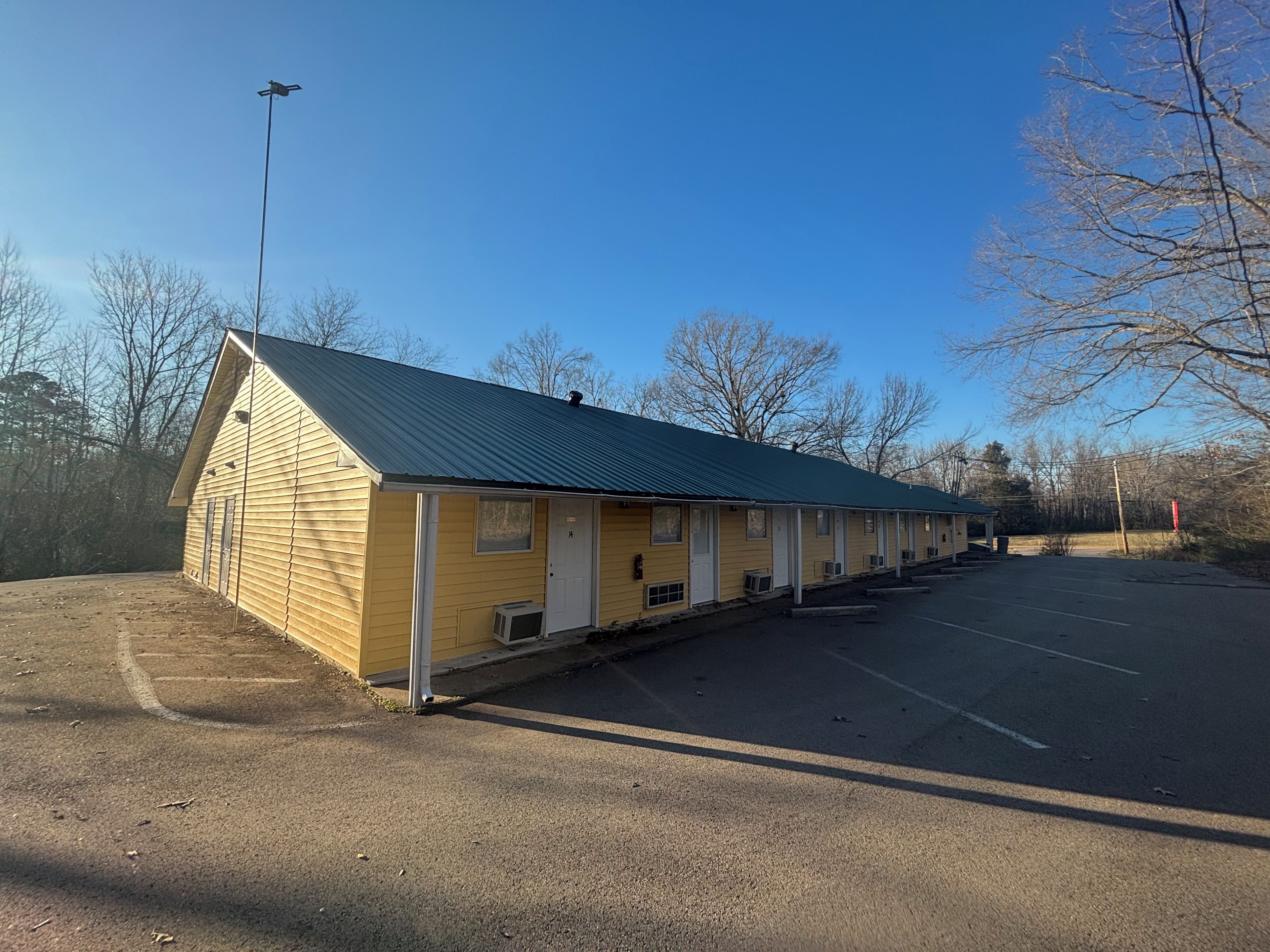 A motel with a row of rooms, a covered parking area, and a clear sky.