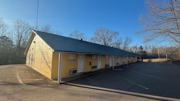 A motel with a row of rooms, a covered parking area, and a clear sky.