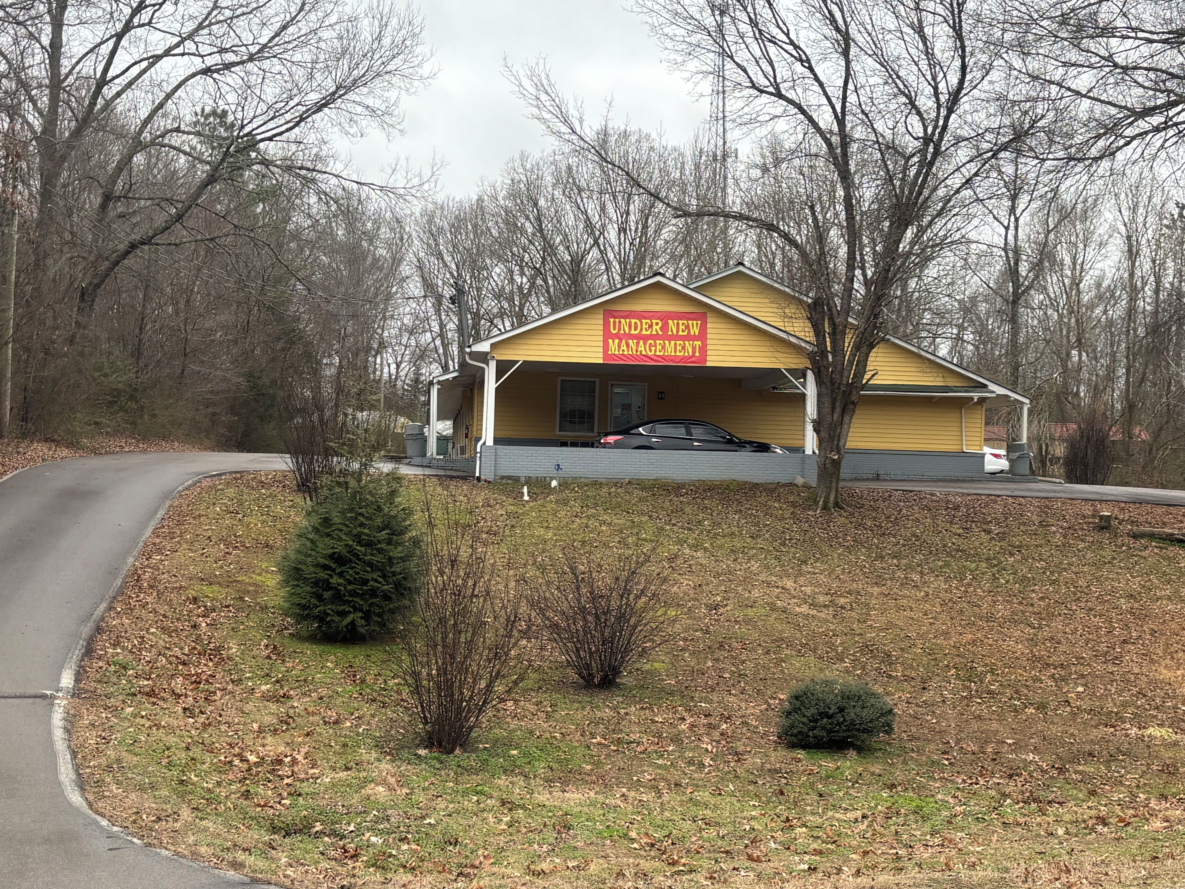 A yellow building with a sign reading 'UNDER NEW MANAGEMENT' in front of a road.