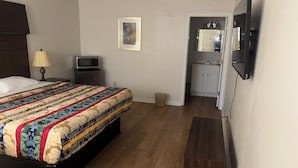A bedroom with a bed, bedside table, lamp, TV, and a view into the kitchen. - Hobson Stay & Residences (Grand Junction)