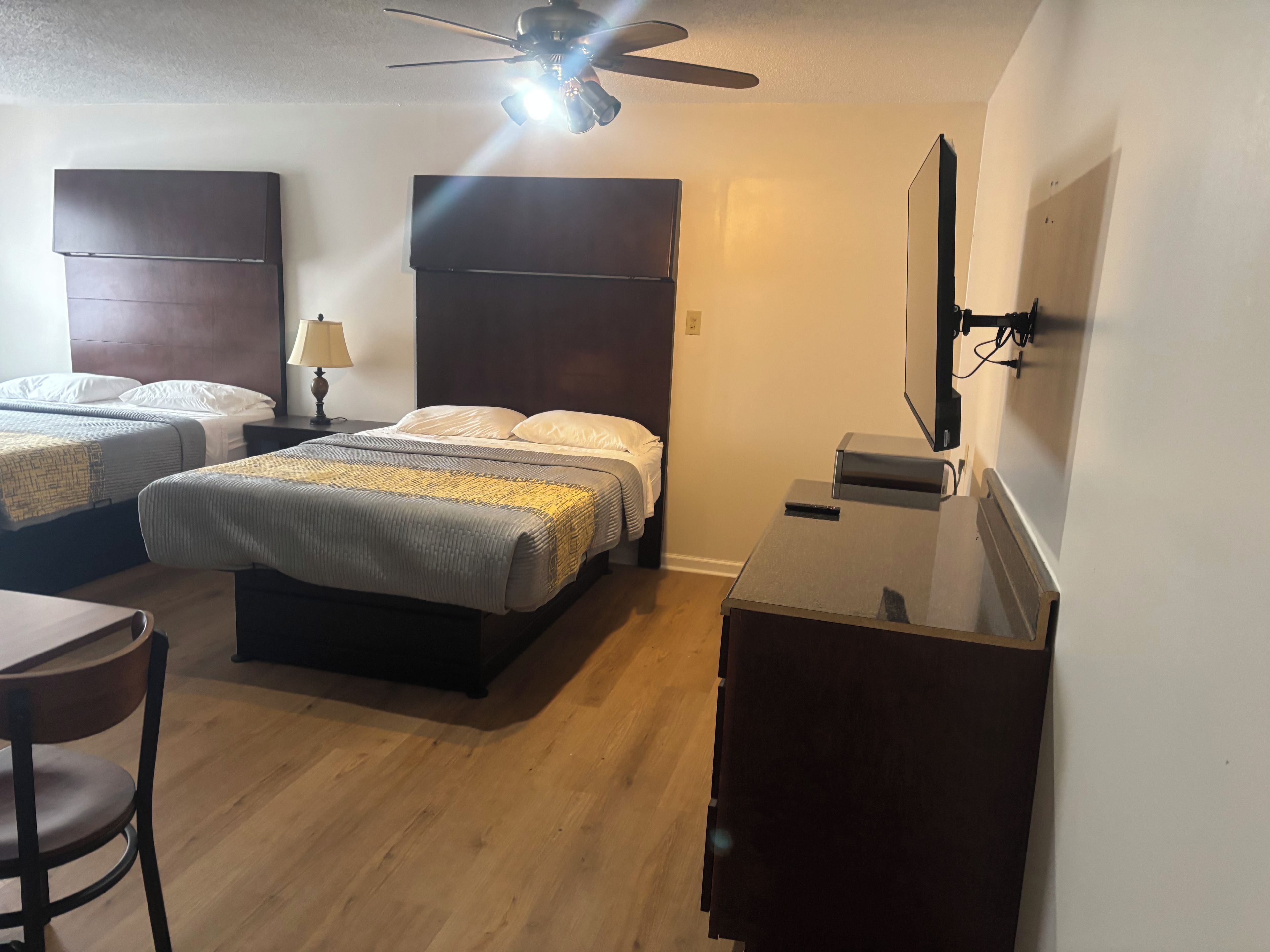 A hotel room with two beds, a desk, a chair, a ceiling fan, and a flat-screen TV.