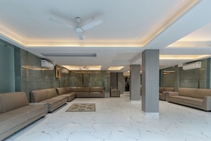 A modern lobby with a sectional sofa, a standing fan, recessed lighting, and marble flooring.