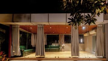 Un espacio habitable interior y exterior con techo de madera, asientos verdes y cortinas.