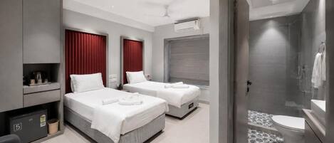 A modern hotel room with two beds, a shower area, and a small seating area.