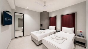 A hotel room with two beds, a television, a mirror, and a ceiling fan. - The Bay Suites - Residency (New Town)