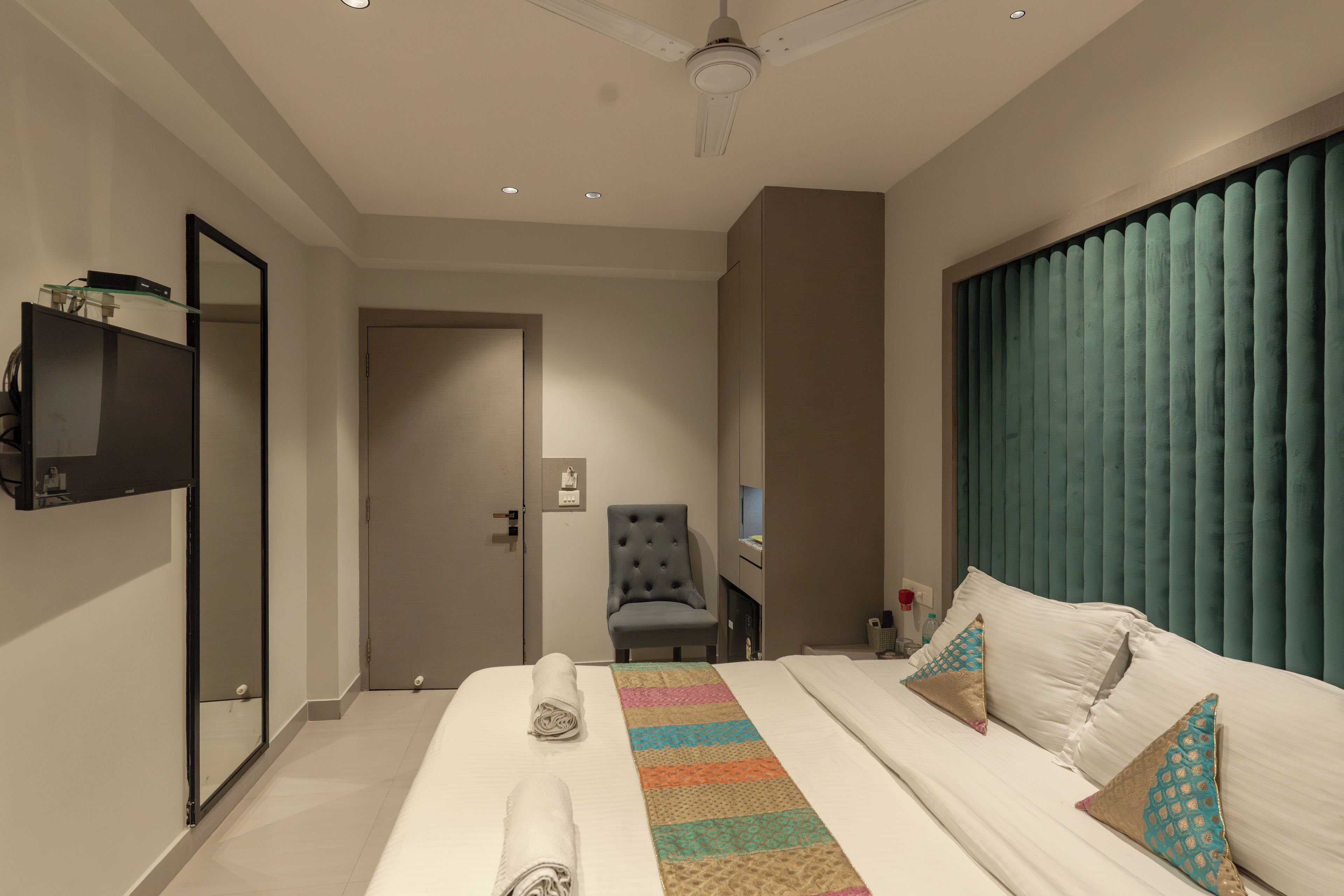 Una habitación de hotel con cama, una silla, un televisor y una ventana con cortinas.