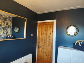 A room with a wooden door, a white radiator, a mirror, and a wall with a circular window. - Hideaway House, Sleeps 6 with Hot Tub & Balcony (Chester Le Street)