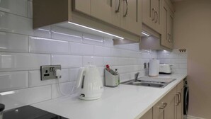 A kitchen with white tiles, a kettle, a toaster, and a coffee machine. - Meigh Village Apartment (Newry)