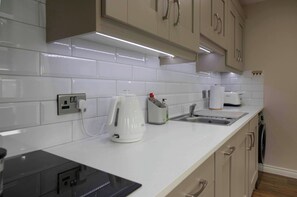 A kitchen with white tiles, a kettle, a toaster, and a coffee machine. - Meigh Village Apartment (Newry)