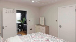 A bedroom with a bed, a dresser, a mirror, and a door leading to a bathroom. - Meigh Village Apartment (Newry)