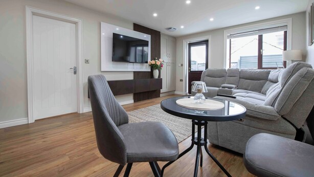 A modern living room with a sofa, chairs, a coffee table, and a flat-screen TV mounted on the wall. - Meigh Village Apartment (Newry)