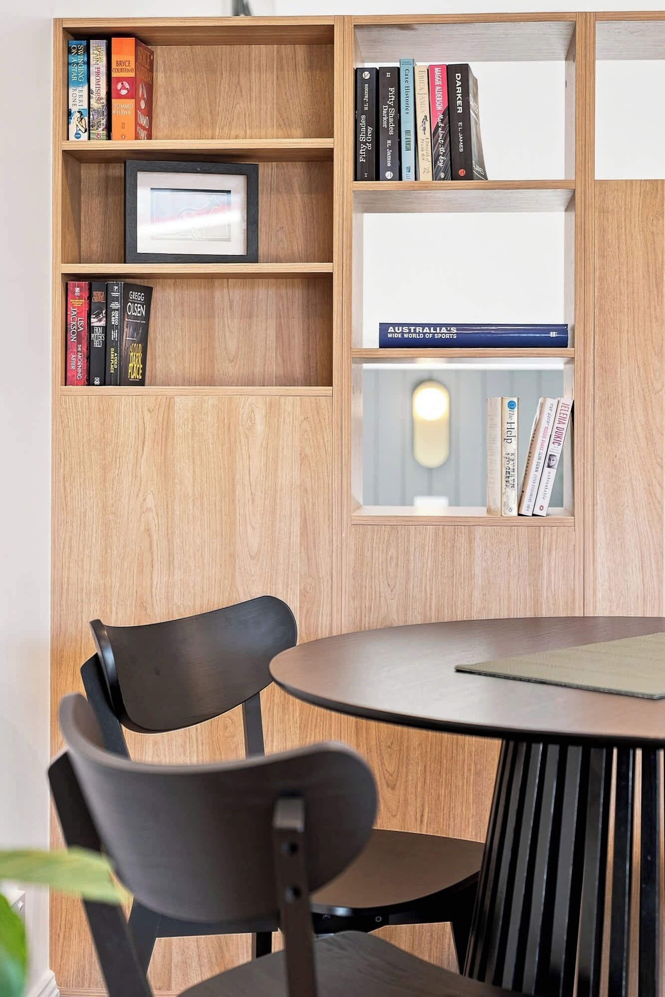 A wooden bookshelf with books, a framed picture, and a table with two chairs.