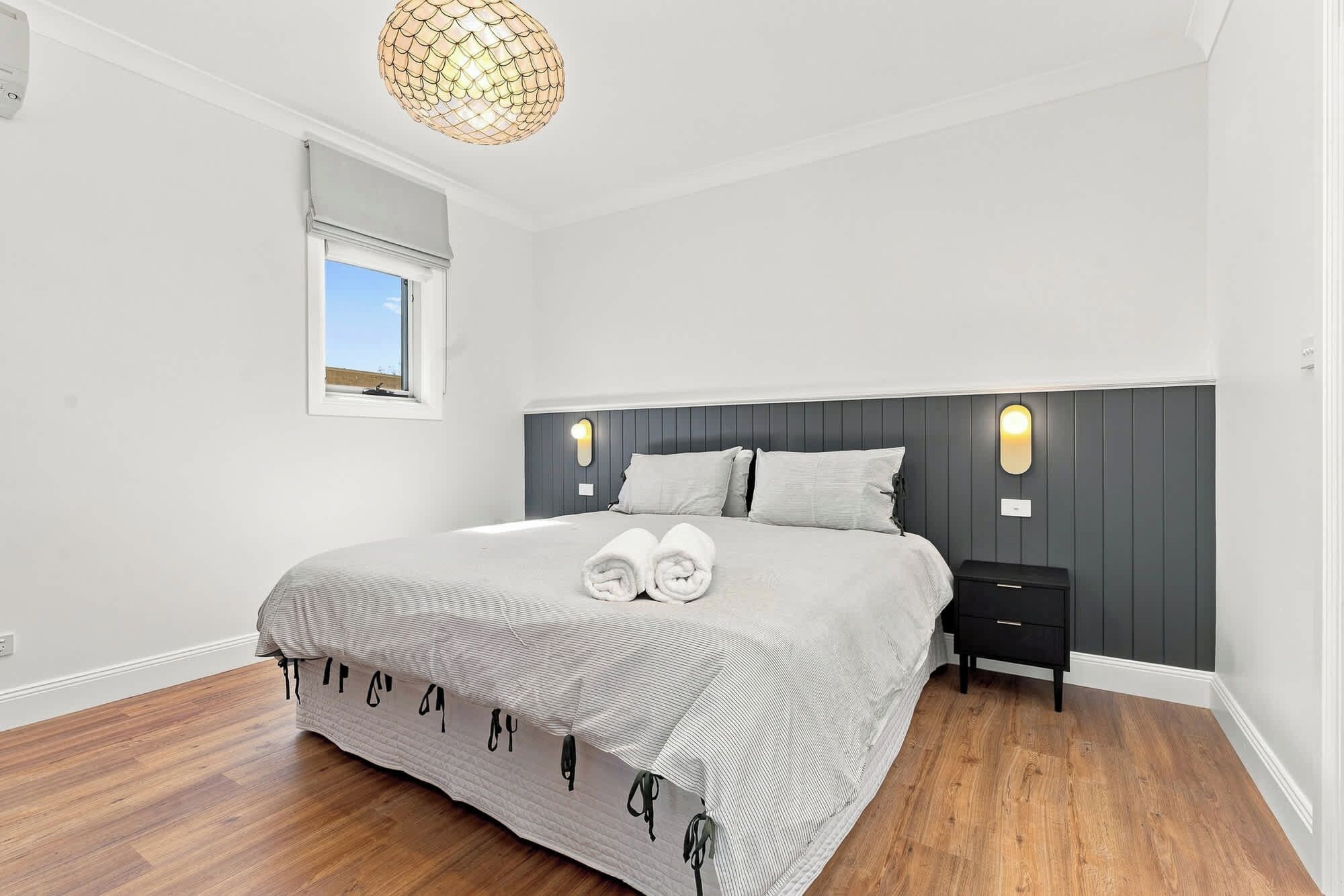 A bedroom with a bed, bedside tables, a hanging light fixture, and a window.