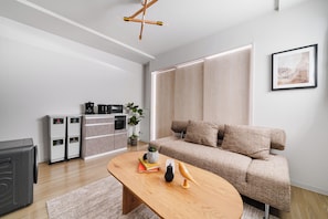A modern living room with a sofa, coffee table, and a kitchen area with appliances. - SONIA 103 (Sapporo)