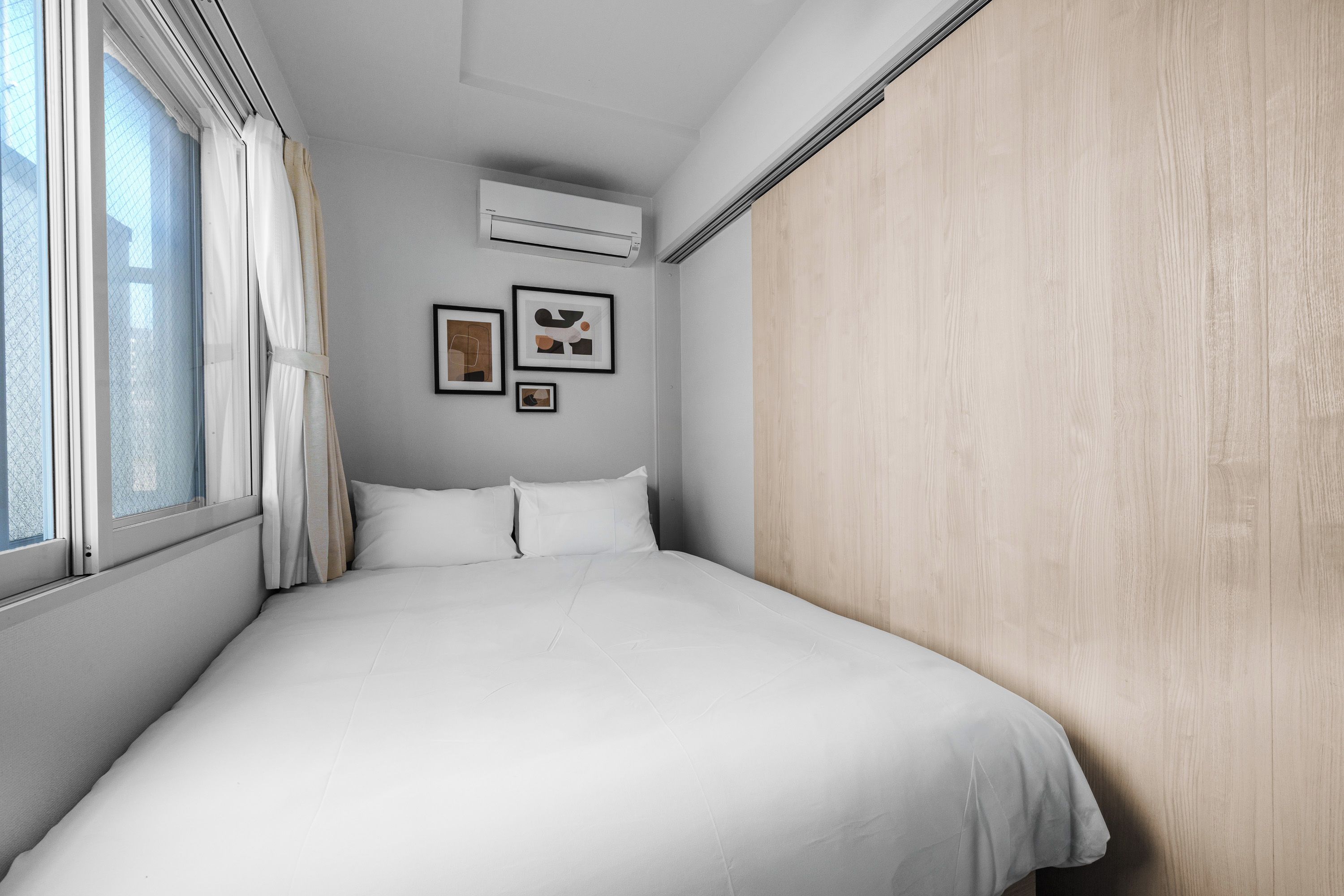 A hotel room with a bed, a window with curtains, and wall-mounted air conditioning.