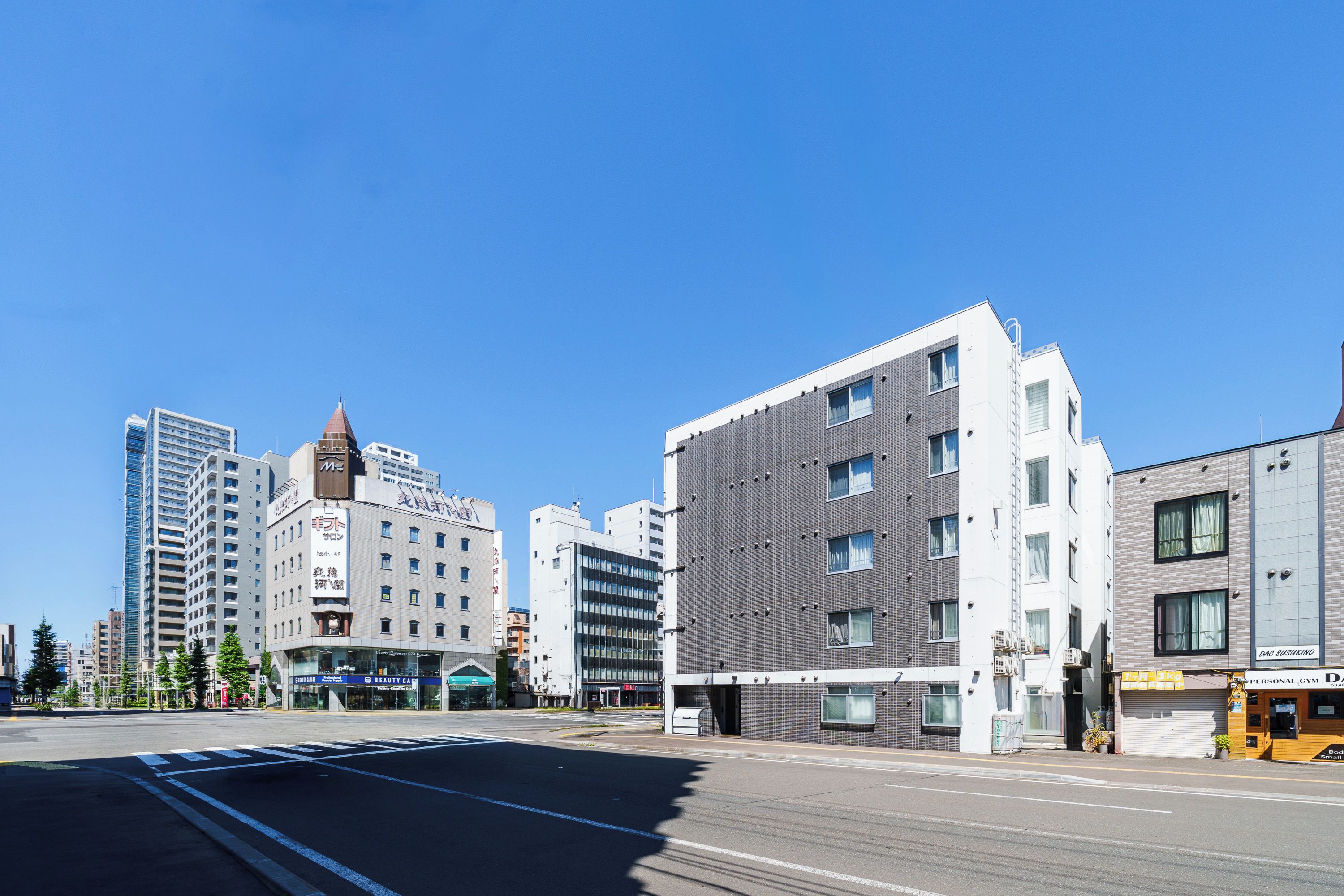 A modern urban street with multi-story buildings, a clear sky, and a crosswalk.