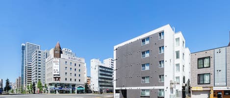 A modern urban street with multi-story buildings, a clear sky, and a crosswalk.