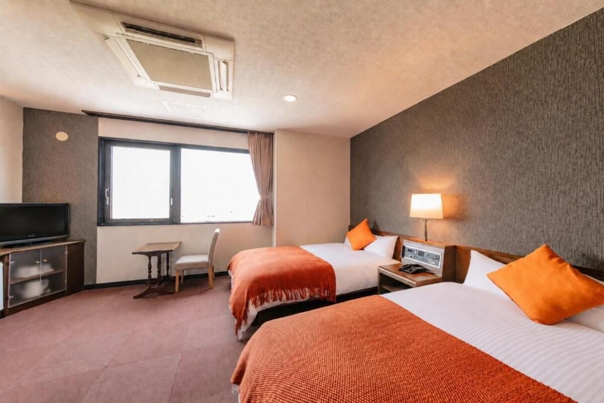 A hotel room with two beds, a television, a desk, and a window.