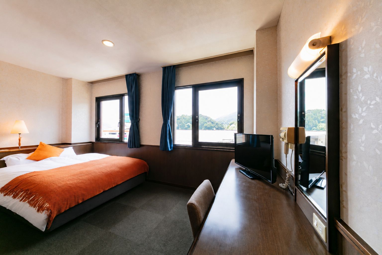 Une chambre d’hôtel avec un lit, un bureau avec une télévision et des fenêtres avec des rideaux.
