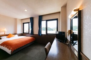 A hotel room with a bed, a desk with a television, and windows with curtains. - Mango Hotel Nichinan (Nichinan City Iwasaki)