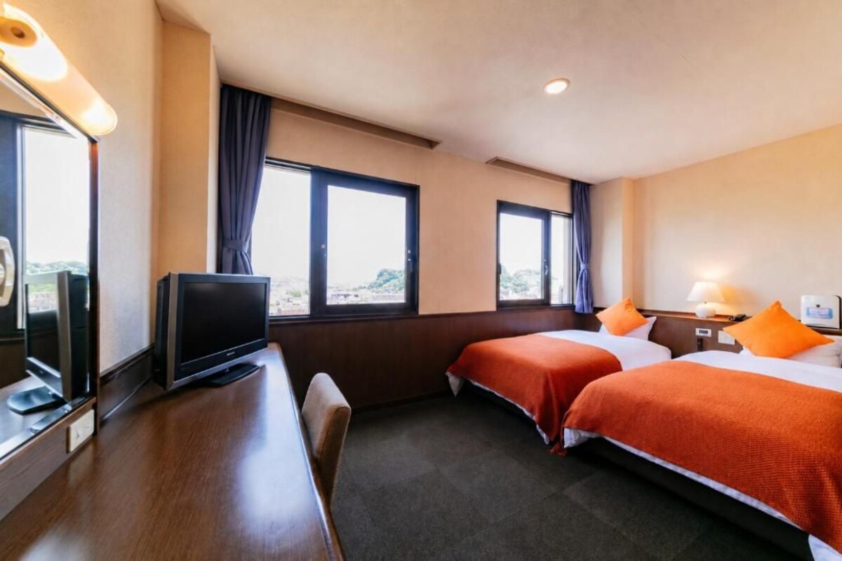 A hotel room with two beds, a desk, a television, and large windows.