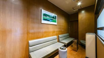 A waiting area with wooden walls, two benches, a framed picture, a trash bin, and a small refrigerator.