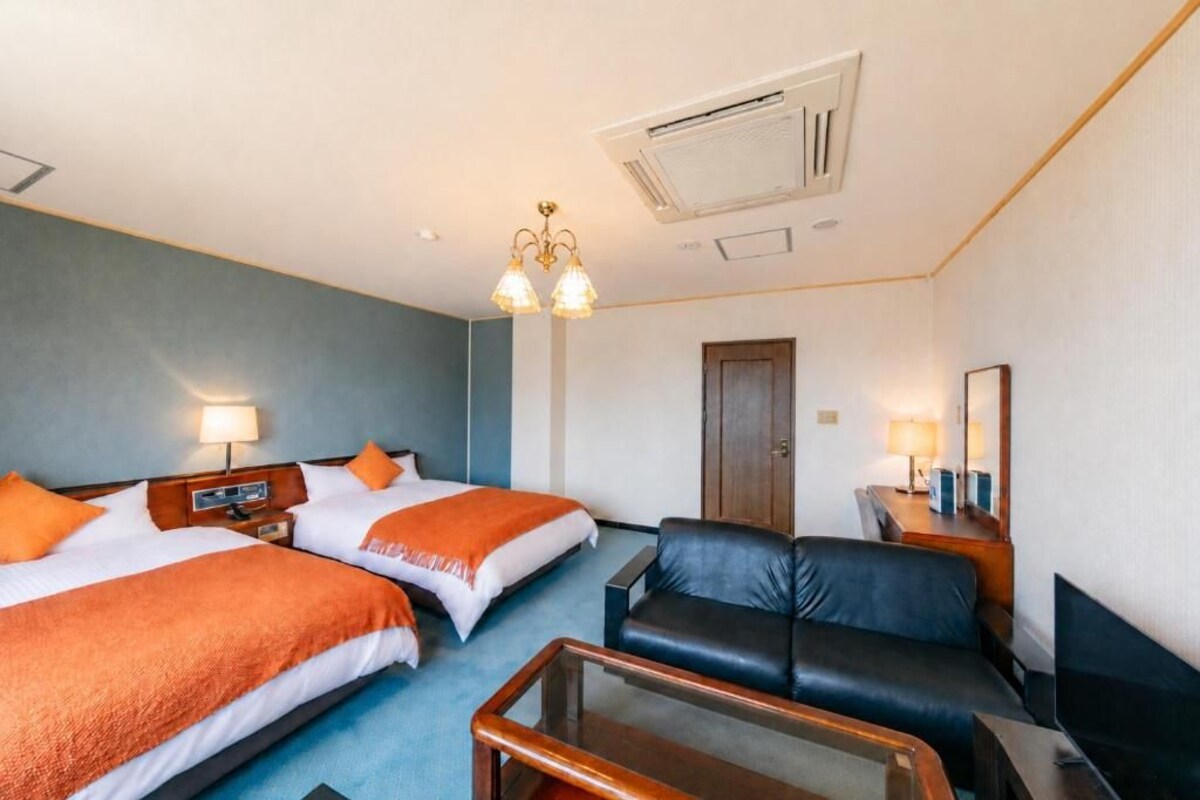 A hotel room with two beds, a sofa, a TV, and a desk with a lamp.